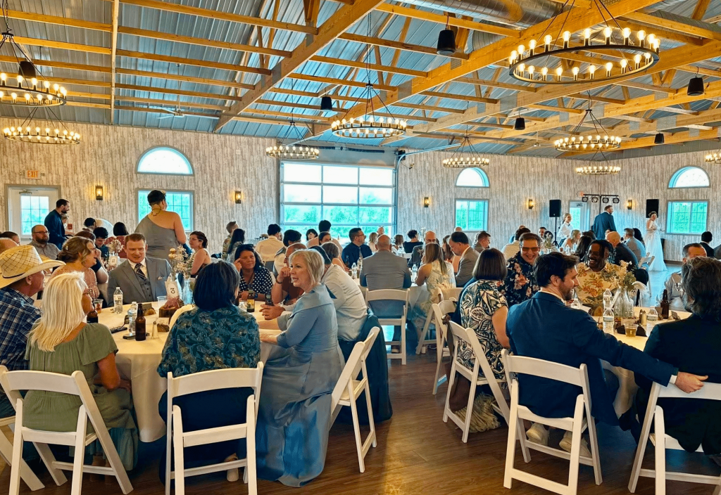 Close look at people sitting at round tables with white chairs in a venue with wooden floors and soft warm lighting.